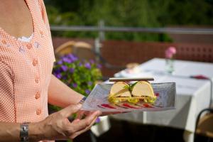 a woman holding a plate with a sandwich on it at Landhotel Traube in Seewald +10 photos