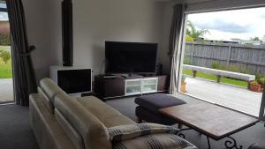 a living room with a couch and a flat screen tv at Cosy Mangawhai House in Mangawhai