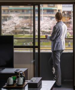 Ein Mann, der aus dem Fenster schaut, auf einen Zug. in der Unterkunft Kyoto Riverview House Kyoraku in Kyoto