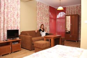 a woman sitting on a couch in a living room at Guest House Stelia in Velingrad