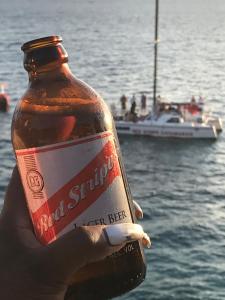 una mano sosteniendo una botella de cerveza con un bote en el agua en Drifters@One Mile en Negril