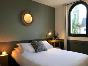 Schlafzimmer mit einem Bett mit einem Spiegel und einem Fenster in der Unterkunft Hotel de France in Saint-Pol-de-Léon