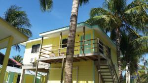 a yellow house with a balcony and palm trees at Barefoot Beach Belize in Caye Caulker