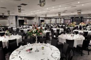 um salão de banquetes com mesas brancas, cadeiras e flores em The Maslow Hotel, Sandton em Joanesburgo
