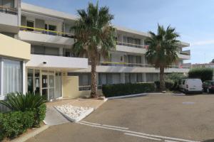 un parcheggio di fronte a un edificio con palme di Sol-y-Days Cigales de mer, studios bien équipés et climatisés, en centre-ville à 150m de la plage a Le Grau-du-Roi