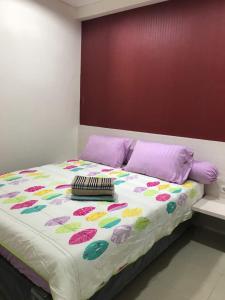 a large bed with a colorful comforter and purple pillows at Apartemen Parahyangan Residence by Rika in Bandung