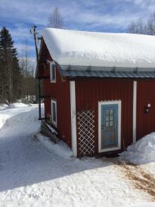 a red house with a snow covered roof in the snow at Stuga Petruslogen in Malung