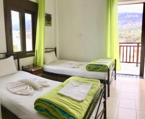 a room with three beds with green curtains and a balcony at Platanos Rooms in Anopoli Sfakion