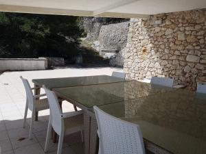a glass table with white chairs and a stone wall at Villa Bocca del Pozzo in Gagliano del Capo