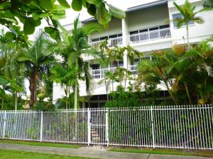 a white fence in front of a building with palm trees at Inner City Oasis in Cairns