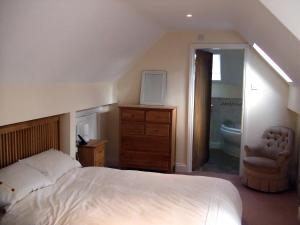 a bedroom with a bed and a chair and a bathroom at Tibbiwell Lodge in Painswick