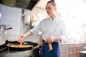 a woman in a kitchen preparing food on a stove at 't VeerHuys in Beusichem