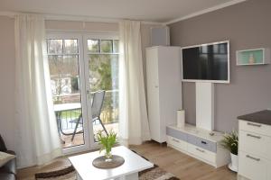 ein weißes Wohnzimmer mit einem TV und einem Fenster in der Unterkunft Villa Ilse in Heringsdorf