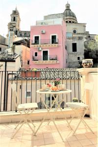 un tavolo e sedie su un balcone con un edificio rosa di Le Luci su Ibla - Ospitalità con vista a Ragusa