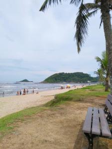 a park bench on a beach with people in the water at CASA - FRENTE PARA O MAR in Itanhaém