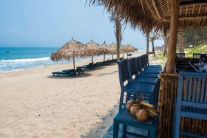 a beach with blue chairs and umbrellas and the ocean at Sol An Bang Beach Resort & Spa in Hoi An