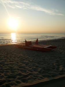 um barco sentado na praia com o pôr do sol em Hotel Paradiso Dei Giovani em Margherita di Savoia