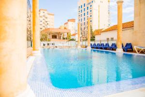 une grande piscine avec des chaises bleues et des bâtiments dans l'établissement Hotel Biarritz, à Gandía