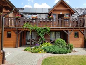 a large wooden house with a deck and flowers at Noclegi na Zaciszu in Kąty Rybackie