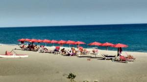 een groep mensen op een strand met rode parasols bij Vista Montagna in Caulonia Marina