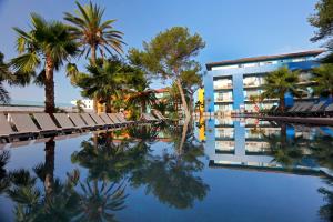 una piscina con palmeras y un edificio en Occidental Menorca, en Punta Prima