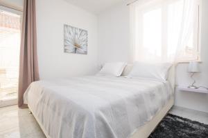 a white bedroom with a bed with white sheets and a window at Concordia Apartments in Dubrovnik