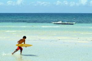 un garçon marchant dans l'eau avec une planche de surf dans l'établissement Masamayor's Beach House and Resort, à Îles Camotes