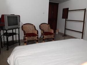a bedroom with a bed and two chairs and a tv at Elroy Homestay in Kalpetta