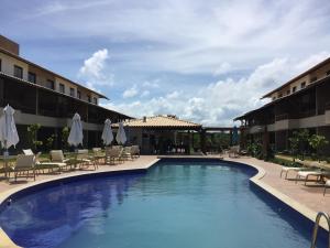 a swimming pool with chairs and umbrellas next to a hotel at Vilage beira mar in Itacimirim