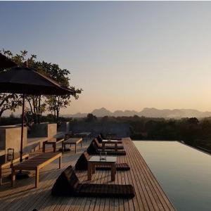 a deck with benches and an umbrella next to a pool at Inchantreedoopool in Kanchanaburi City