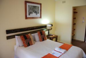 a bedroom with a bed with white sheets and orange pillows at Journey's Inn Africa Airport Lodge in Kempton Park