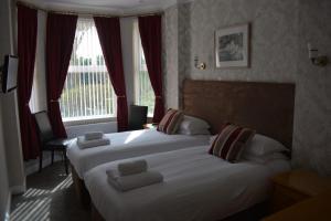 two beds in a hotel room with red curtains at Cotswold House in Falmouth