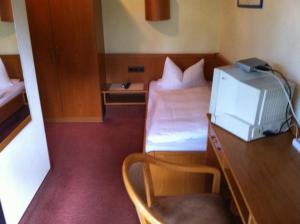 Habitación pequeña con cama y escritorio con TV. en Hotel Bacchusstube garni, en Goldbach