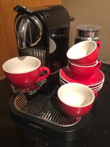 - une cafetière avec quatre tasses et assiettes rouges dans l'établissement Hotel Le Baroudeur, à Fauquemont