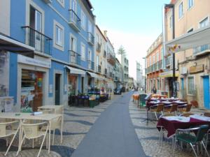 an empty street with tables and chairs and buildings at Bem Me Quer in Almada