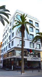 a large white building with a palm tree in front of it at Hotel Centre Ville in El Jadida