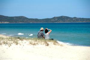 un hombre y una mujer sentados en la playa mirando el agua en Villetta Valeria en Costa Rei