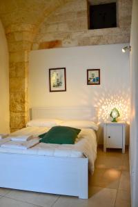 Cama blanca en habitación con pared de piedra en La Violetta Ostuni, en Ostuni