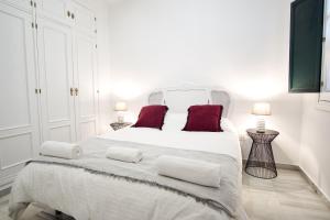 um quarto branco com uma grande cama branca com almofadas vermelhas em Monsalves Courtyard by Valcambre em Sevilha