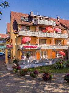 un grand hôtel avec des parasols rouges devant lui dans l'établissement Strandpension Mäder, à Uhldingen-Mühlhofen