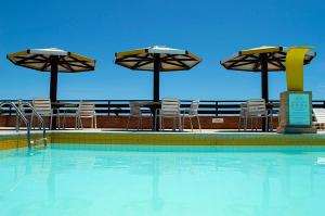 a swimming pool with chairs and umbrellas and a table and chairs at Apartamento Pipa Deluxe in Pipa