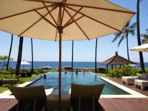 a swimming pool with an umbrella and people in the water at The Amrita - Salt Farm Villas in Tejakula