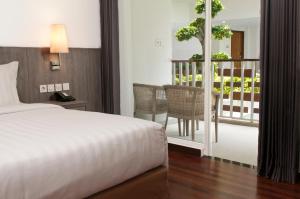 a bedroom with a bed and a balcony with a table at ASTON Canggu Beach Resort in Canggu