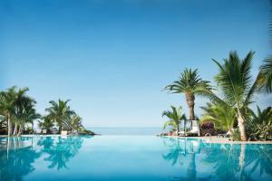 uma piscina com palmeiras e o oceano em Adrián Hoteles Roca Nivaria em Adeje