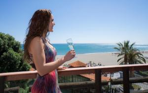 a woman holding a glass of wine in front of a beach at Hotel MS Tropicana in Torremolinos