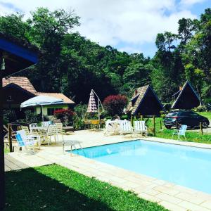 una piscina con sillas, una mesa y un coche en Pousada Cabanas do Visconde, en Visconde De Maua