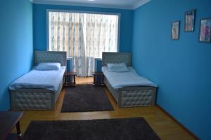 two beds in a room with blue walls and a window at Golden Apartments in Khujand