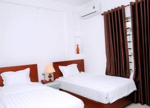 two beds in a room with white sheets and brown curtains at Sunflower Hotel in Ninh Binh