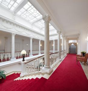 a large white hall with a red carpet and columns at Imperial Spa & Kurhotel in Františkovy Lázně