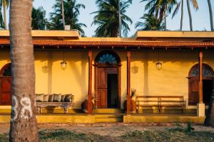 a yellow house with a bench and palm trees at Luna Laguna in Kalpitiya
